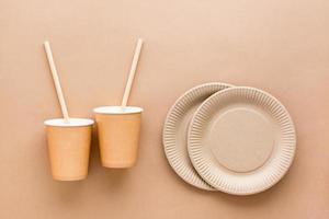 Cardboard cups, drinking straws and plates on a beige background. Eco friendly and zero waste concept. Top view. photo
