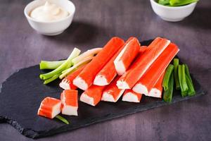 Spicy crab sticks and green onions on a stone board and sauce in a bowl on the table photo