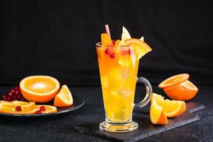 naranja arándano gaseoso cóctel en un vaso y frutas siguiente a eso en un oscuro antecedentes. hecho en casa Mocktail foto