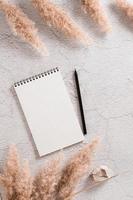Notebook, pencil and fluffy dry grass on a textured background. Planning and goals. Eco background. Top and vertical view. photo