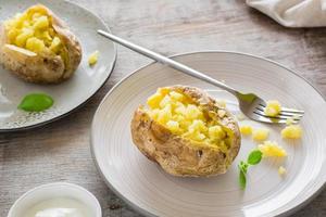 Baked potatoes in their skins on plates and a bowl of sour cream on a wooden table. Vegetarian natural food. Close-up photo