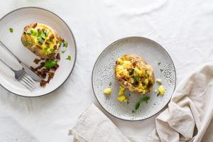 horneado dos veces patatas en su Pieles con queso y tocino migas en platos en un de madera mesa. flexitariano dieta. parte superior ver foto