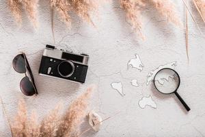 Flat lay concept travel. Vintage camera, sunglasses, continent templates and magnifier on textured concrete background.