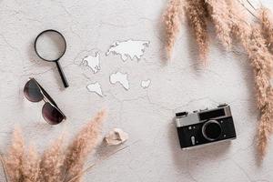 Flat lay concept travel. Continents templates, magnifier, vintage camera and sunglasses surrounded by grass on textured concrete background. photo