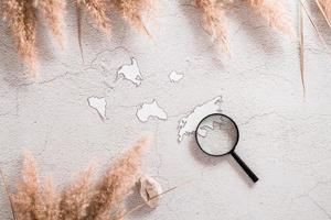 Flat lay concept travel. Continent templates and magnifying glass in grass cover on textured concrete background. photo