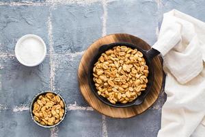 Fresh roasted peanuts in a frying pan, salt and oil on the table. Plant source of protein. Vegetarian food. Top view photo