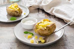 horneado patatas en su Pieles y un cuenco de agrio crema en un plato en un de madera mesa. vegetariano natural comida foto