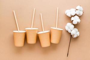 Cardboard cups, drinking straws and a branch of cotton on a beige background. Eco friendly and zero waste concept. Top view. photo