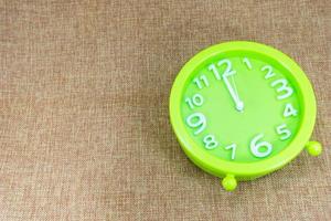 Green alarm clock on brown sackcloth background show 12.00 a.m. photo