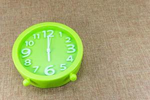 Green alarm clock on brown sackcloth background show Six o'clock or 6.00 a.m. photo