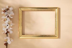 Empty golden frame with delicate cherry petals on a beige background photo