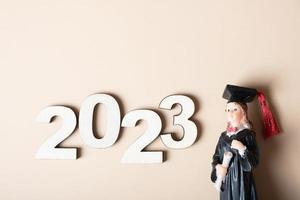 Class of 2023 concept. Wooden number 2023 with graduate statuette on color background photo