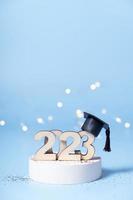 Class of 2023 concept. Wooden number 2023 with graduated cap on podium on colored background photo