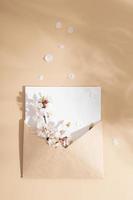 An envelope with delicate cherry blossom petals on a beige background. Spring vertical mock up photo