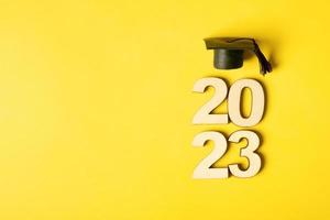 Class of 2023 concept. Wooden number 2023 with graduated cap on colored background photo