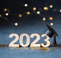 Class of 2023 concept. Wooden number 2023 with graduate cap on dark background with bokeh photo