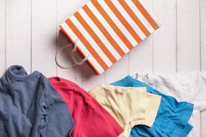 Colorful clothing and shopping bag on wooden background. Second hand, recycling concept photo