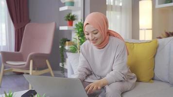feliz muçulmano mulher trabalhando em computador portátil e sorridente. muçulmano mulher dentro hijab olhando às computador portátil e feliz. video
