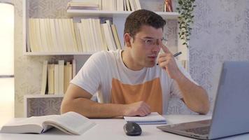 travail Université étudiant concentré sur le sien leçon. se concentrer sur le sien leçon, le étudiant travaux sur une portable. il a une livre et une carnet dans de face de lui. video