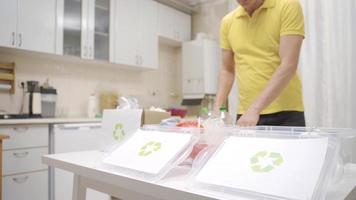 persona lanzamiento residuos dentro reciclaje contenedores en el cocina. el hombre ordena el residuos papel, el plastico y vaso en el cocina para reciclaje y pone ellos en cajas video