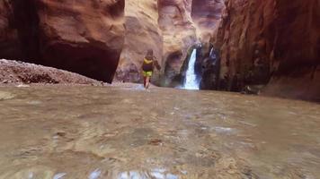hembra turista caminar en agua en famoso río cañón de cauce mujib en increíble dorado ligero colores. cauce mujib viaje destino en Jordán. submarino acción cámara pov video