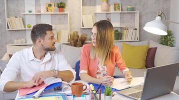 Married couple working in home office. The woman working at the desk and her husband in the back are reading a book. video