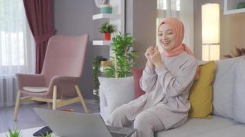 musulmano giovane donna guardare a il computer portatile e gioire. musulmano donna nel hijab guardare a il computer portatile sorpreso e contento. video