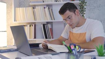 Universität Schüler lesen ein Buch. das Schüler ist lesen ein Buch beim heim. er hat Laptop und Bücher auf seine Schreibtisch. video