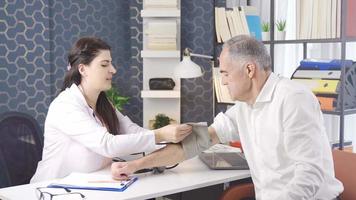 Professional female doctor sitting at office desk and measuring blood pressure of patient. The female doctor measures the blood pressure of her elderly patient and warns her. video