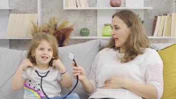 el madre es jugando el médico juego con su hija quien quiere a ser un doctor. el pequeño niña escucha a su madre con un estetoscopio y ella disfruta eso con placer. video