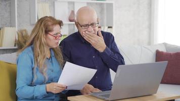 The old couple is saddened by the bad news. The elderly couple receives sad news in a paperwork they are looking at. video