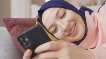 Satisfied Muslim girl wearing hijab is using smartphone at home. Muslim girl looking at her smartphone. video