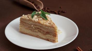 Close up of Delicious Napoleon Cake with cream on a white plate decorated with a sprig of mint on a Brown Background. A cinnamon stick, badyan, coffee beans on a brown background. Copy space video