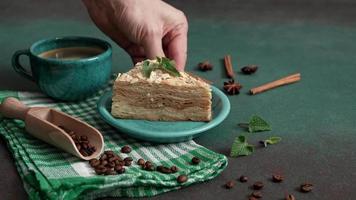 homme main met en haut turquoise assiette de Frais délicieux gâteau napoléon avec crème sur une vert Contexte. une cannelle bâton, Badyan, café des haricots sur une vert tableau. copie espace video