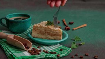 Man's hand with fork breaks off piece of Fresh delicious Cake Napoleon with cream on a Green Background. A cinnamon stick, badyan, coffee beans on a brown background. Copy space video