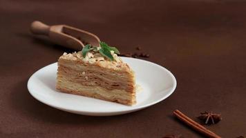 proche en haut de en couches gâteau avec crème napoléon avec menthe sur marron Contexte. une cannelle bâton, Badyan, café des haricots sur une marron Contexte. copie espace video