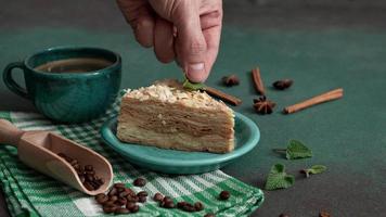 Pastry chef's Hand decorate with mint leaves Fresh delicious Cake Napoleon with cream on a Green Background. A cinnamon stick, badyan, coffee beans on a brown background. Copy space video