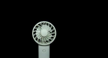 Small useful hand or desk white fan photo isolated on dark black background. Simple technology for cooling breezing air at the office or home.