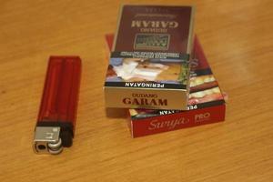 Jakarta, Indonesia - March 12, 2023 - Couple of Gudang Garam cigarettes packs next to red lighter on wooden desk surface area. photo