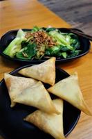 Samosas on a black plate as a close up with green vegetables in the background photo