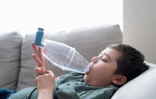 Sick child using asthma inhaler for allergies,Poor boy tired from chest coughing holding inhaler spacer,Tried Kid having asthma allergy photo