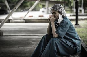 Tired depressed female asian scrub nurse wears face mask blue uniform sits on hospital floor,Young woman doctor stressed from hard work photo