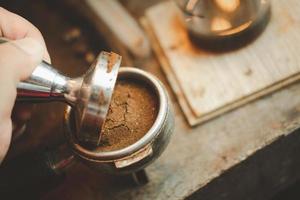 Barista using a tamper to press ground coffee into a portafilter photo