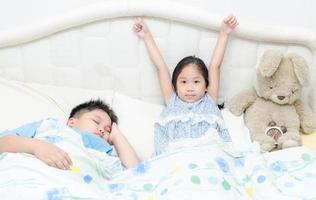 adorable pequeño linda niña despierto arriba en su cama y hermano dormir foto