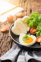 fried eggs and bread in the shape of a heart and fresh vegetables with blank notebook. photo