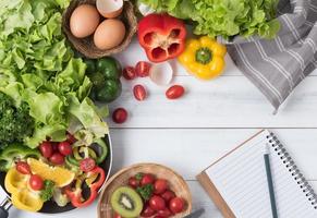 Fresh salad vegetables and fruit with notebook and pencil photo