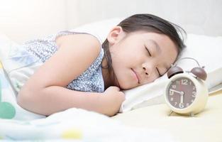 linda niña dormir en cama con alarma reloj. foto