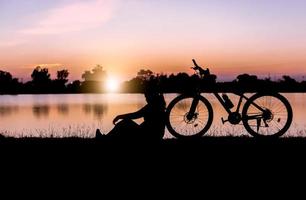 silueta mujer sentar cerca bicicleta en puesta de sol. foto