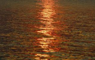 agua superficie con luz de sol en puesta de sol. foto