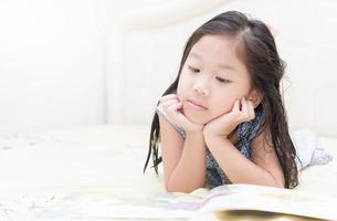 Cute little asian girl in nightdress reading a book. photo